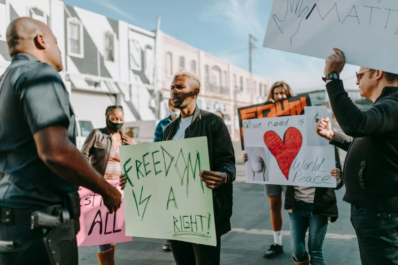 a group of people holding signs in the street, by Julia Pishtar, trending on pexels, black arts movement, gay rights, background image, freedom fighter, a person standing in front of a