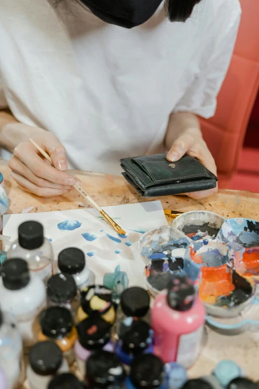 a woman sitting at a table working on a painting, an airbrush painting, trending on pexels, holding a leather purse, smeared acrylic paint, inspect in inventory image, ink paint