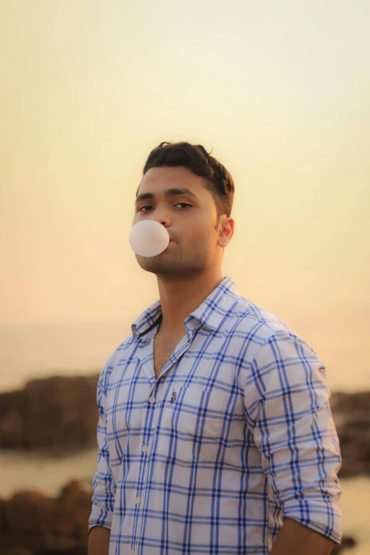 a man blowing a bubble while standing next to a body of water, profile image, desi, marshmallow, standing near the beach