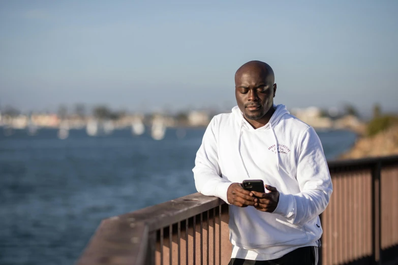 a man standing on a bridge looking at his cell phone, a portrait, by Anthony S Waters, happening, wearing a purple sweatsuit, long beach background, avatar image, lance reddick