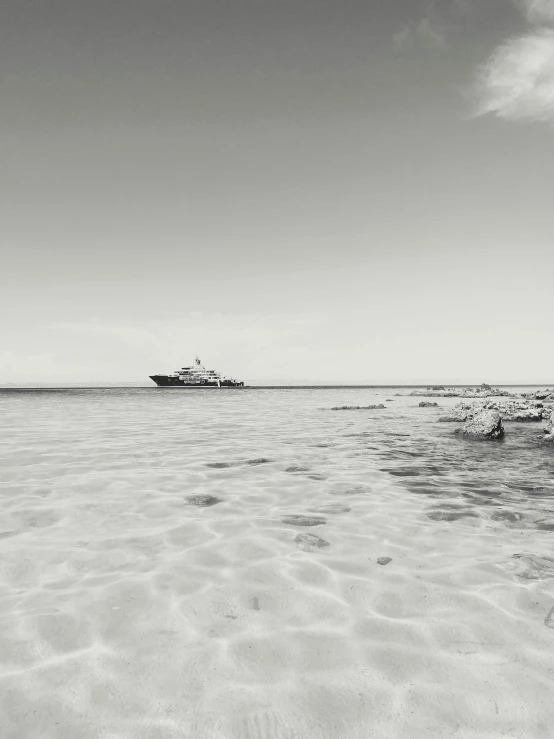 a black and white photo of a boat in the ocean, by Andrew Bell, white sandy beach, on a super yacht, red sea, with a long white