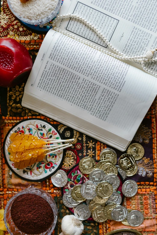 an open book sitting on top of a table, inspired by Li Di, pexels contest winner, qajar art, snacks, pray, gold coins, full frame image