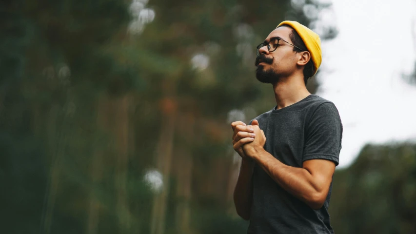 a man with a yellow hat standing in front of a forest, pexels contest winner, praying meditating, hipster dad, man with glasses, high quality product image”