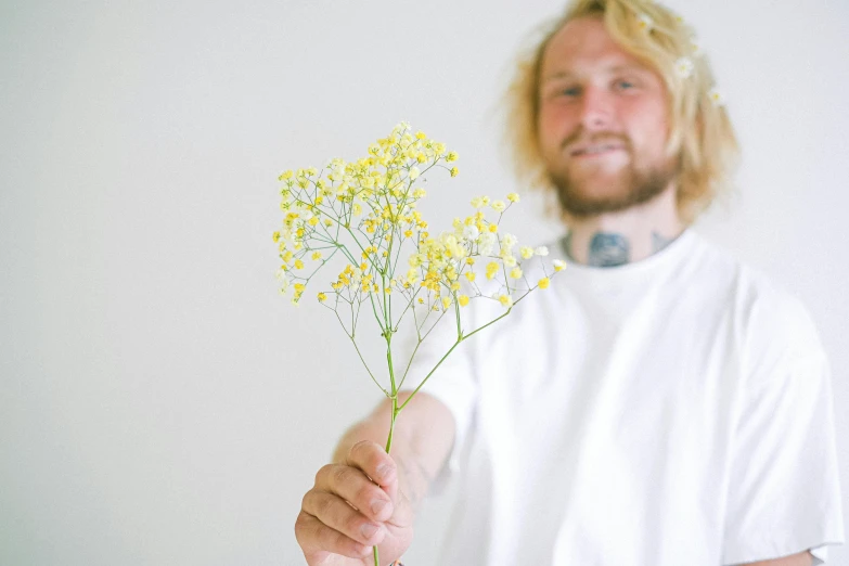 a man holding a bunch of flowers in his hand, an album cover, inspired by Samu Börtsök, unsplash, aestheticism, medium yellow blond hair, bam margera, gypsophila, on a white table