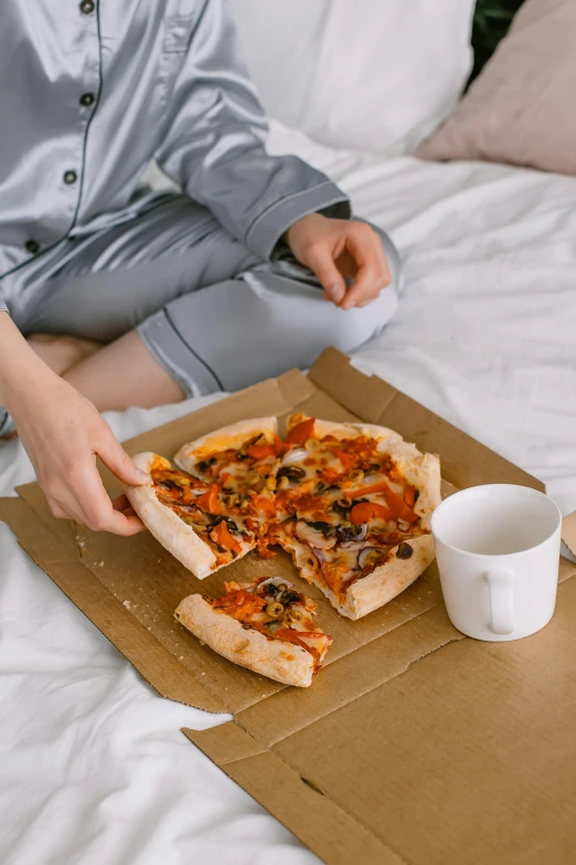 a woman sitting on a bed eating a pizza, by Julia Pishtar, pexels contest winner, cardboard, wearing a grey robe, 👅 👅, overflowing with baked beans