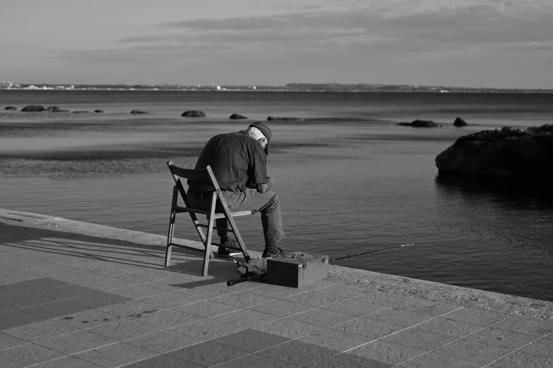 a man sitting on a chair next to a body of water, a black and white photo, pexels contest winner, precisionism, old man doing hard work, japan shonan enoshima, 15081959 21121991 01012000 4k, sculptor