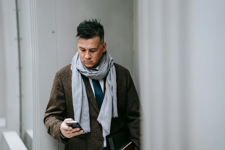 a man standing in a hallway looking at his cell phone, pexels contest winner, wearing a scarf, in gunmetal grey, smart casual, owen gent