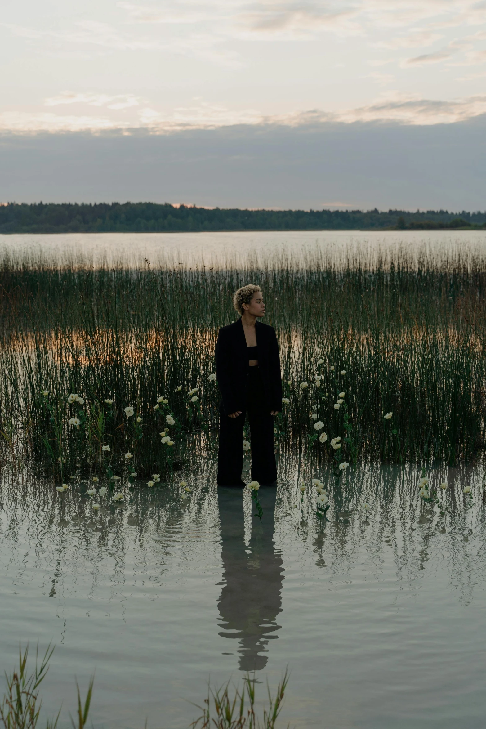 a woman standing in a body of water, an album cover, by Caro Niederer, lake house, woman in black robes, instagram post, evening lights