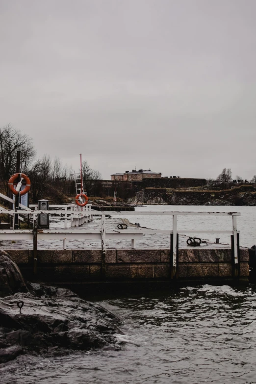 a man standing on top of a pier next to a body of water, a picture, by Jesper Myrfors, stormy snowy weather, low quality photo, lock, they are close to each other