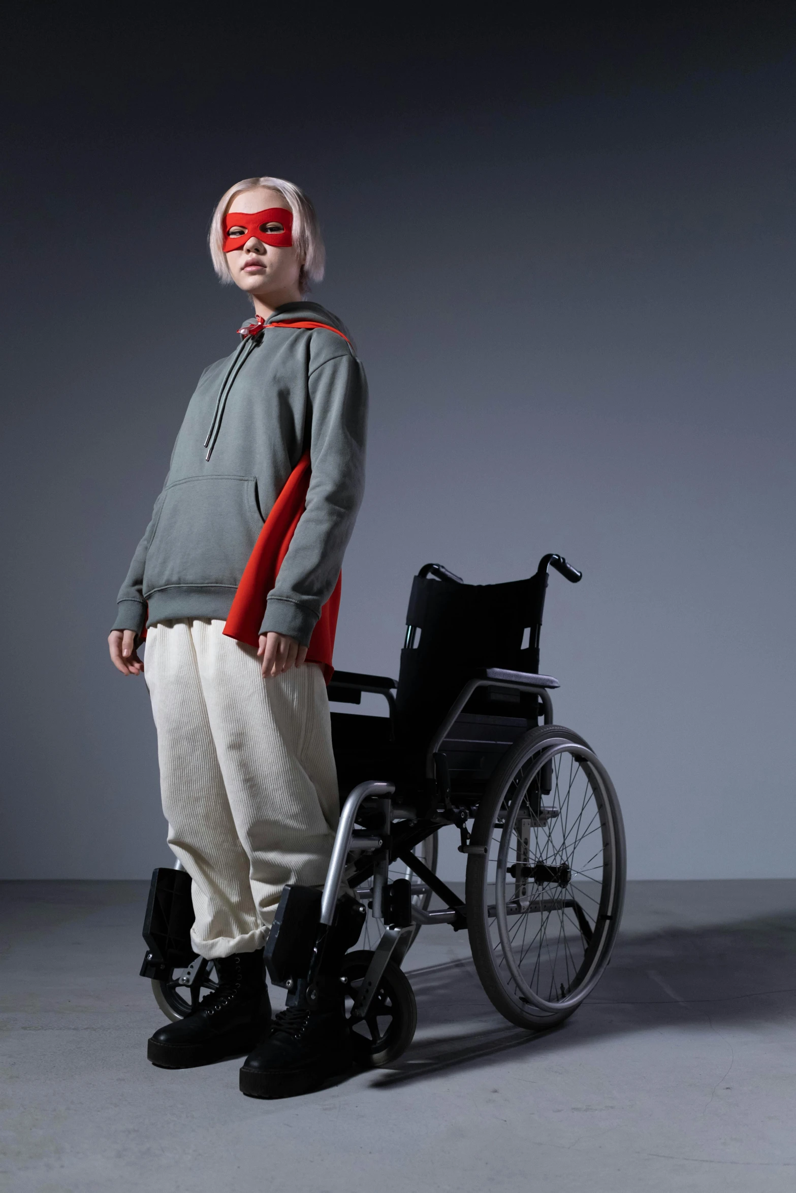 a man with a blindfold standing next to a wheelchair, an album cover, by Hiroyuki Tajima, wearing a hoodie and sweatpants, wearing hero costume, editorial photograph, teenage girl