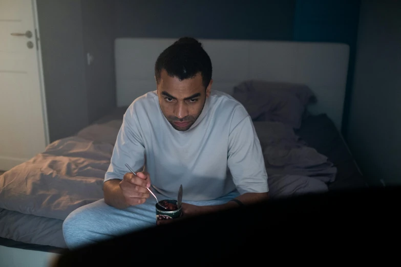 a man sitting on a bed eating food, happening, netflix, early night, riyahd cassiem, looking at monitor