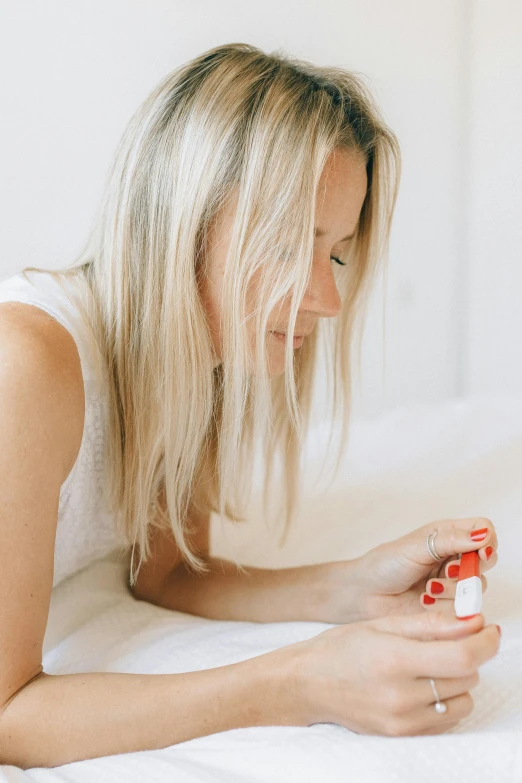 a woman laying on a bed using a cell phone, by Olivia Peguero, trending on pexels, minimalism, holding hot sauce, red and white color scheme, close up of a blonde woman, profile image