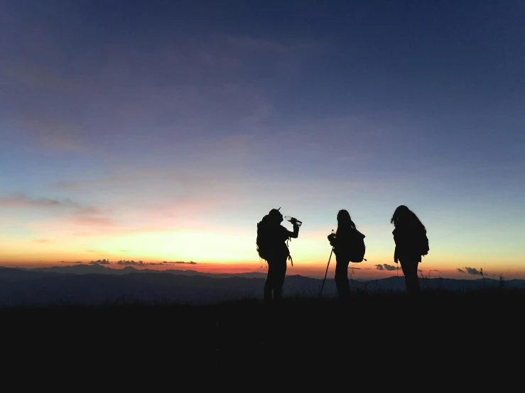 a couple of people standing on top of a mountain, pexels contest winner, dusk sky, adventuring party, silhouettes in field behind, drinking
