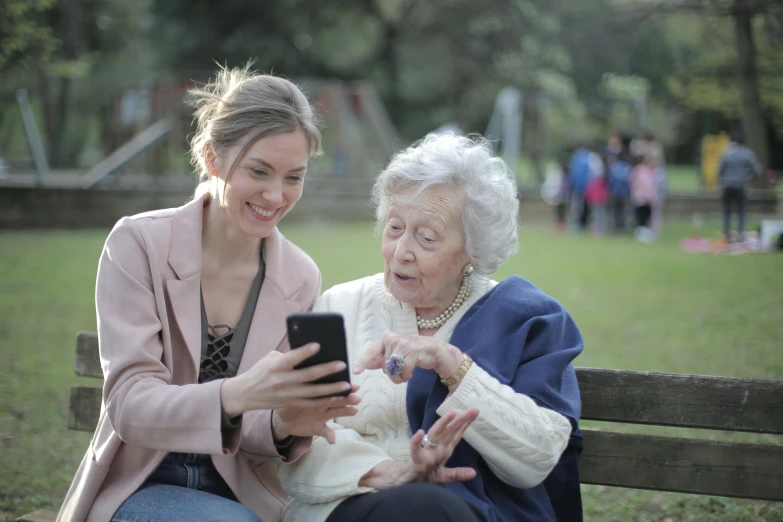 a woman sitting next to an older woman on a bench, hold up smartphone, te pae, unedited, very professional