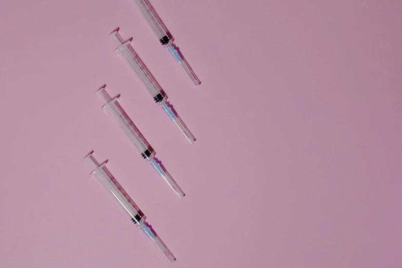 a group of sylls sitting on top of a pink surface, by Matija Jama, trending on pexels, syringes, background image, her iridescent membranes, syringe