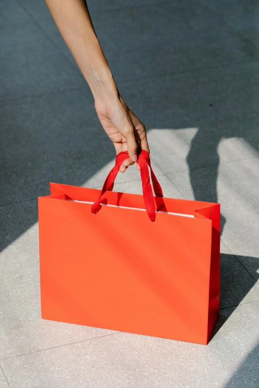 a person holding a red shopping bag on a sidewalk, coral red, cardstock, no text, orange ribbons