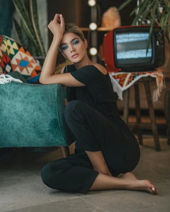 a woman sitting on the floor in front of a couch, a colorized photo, trending on pexels, black outfit, jumpsuit, cinematic outfit photo, beautiful mexican woman