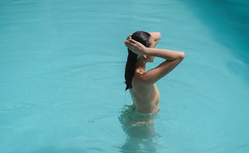 a woman standing in the middle of a swimming pool, light blue water, showing her shoulder from back, seraphine, qualia