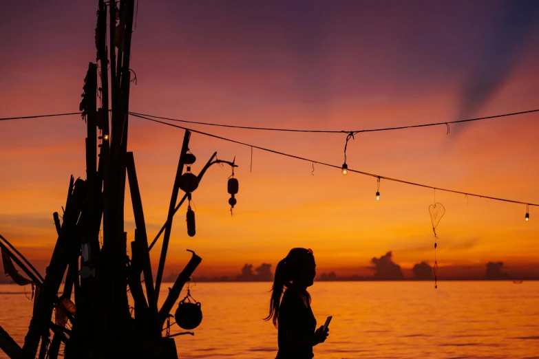 a silhouette of a person standing in front of a body of water, pexels contest winner, sumatraism, fishing village, avatar image, warm coloured, girl under lantern