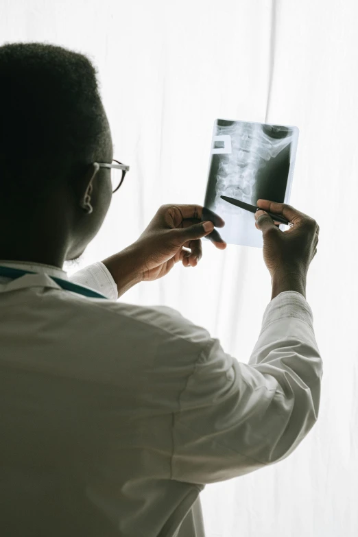 a man standing in front of a window looking at an x - ray, a picture, pexels contest winner, showing her shoulder from back, black human spine, on an operating table, with a stethoscope