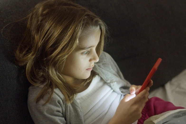 a little girl sitting on a couch looking at a cell phone, pexels, nightlight, natalia dyer, getty images, multicoloured