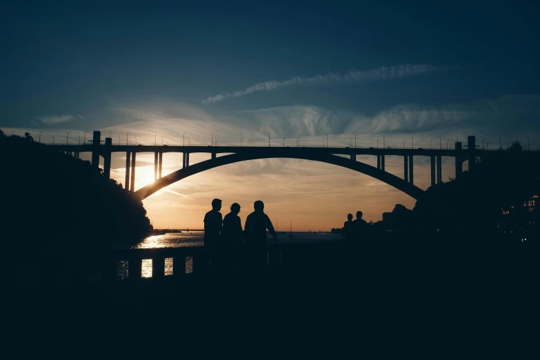 a group of people standing in front of a bridge, by Niko Henrichon, pexels contest winner, romanticism, oceanside, backlit, afternoon hangout, calm evening