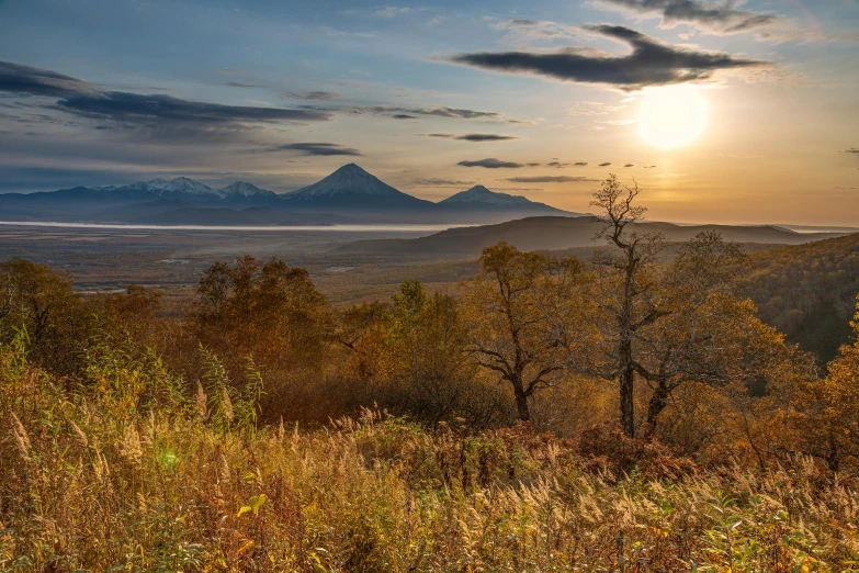 the sun is setting over the mountains in the distance, unsplash contest winner, land art, autumn foliage in the foreground, norilsk, volcanoes in the background, overlooking a valley with trees