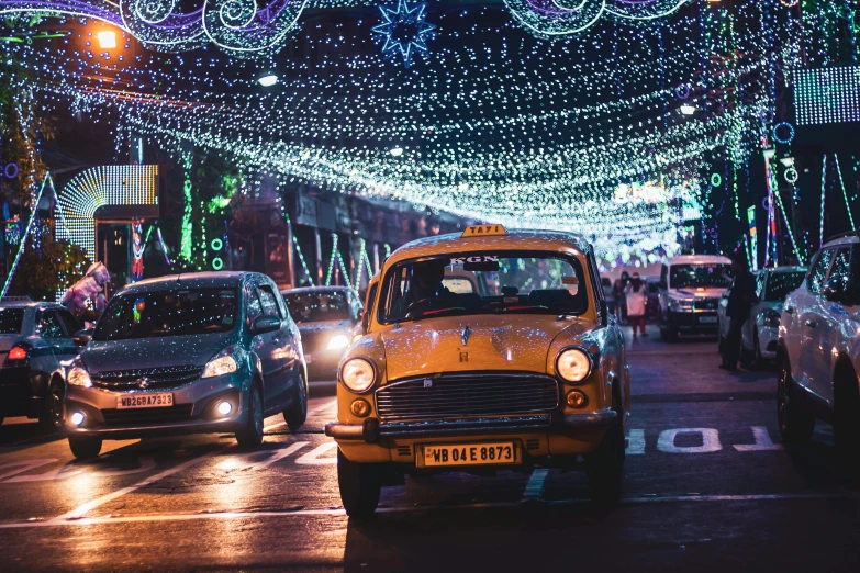 a group of cars driving down a street covered in christmas lights, by Julia Pishtar, pexels contest winner, on an indian street, taxi, lada, promo image