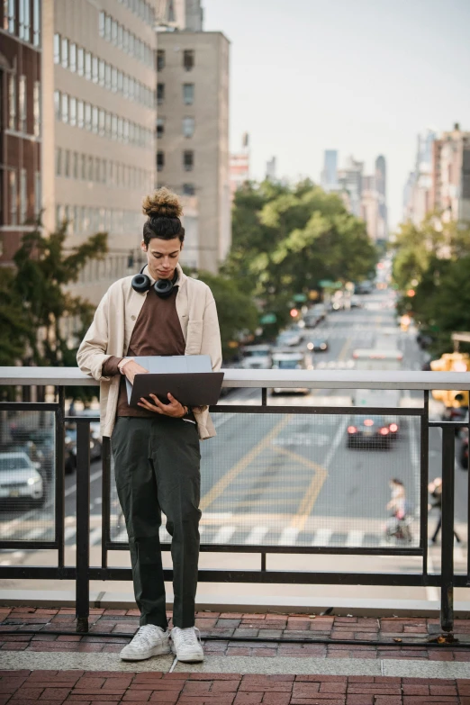 a man standing on a balcony with a laptop, by Nina Hamnett, trending on unsplash, happening, humans of new york, he is holding a large book, androgynous male, streetscape