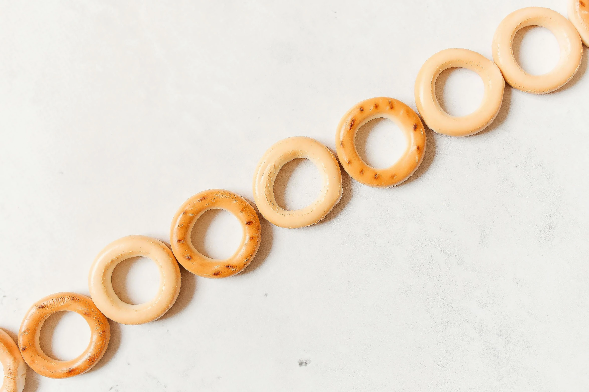 a row of wooden donuts on a white surface, by Nicolette Macnamara, trending on pexels, made of swiss cheese wheels, circlet, natural soft rim light, made of bamboo