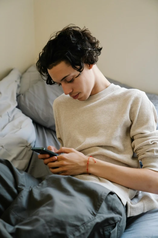 a man sitting on a bed looking at his cell phone, inspired by Nan Goldin, trending on pexels, renaissance, finn wolfhard, gay, tom holland, afternoon