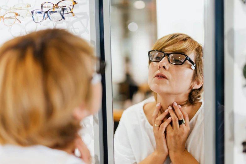 a woman looking at her reflection in a mirror, trending on pexels, hurufiyya, wearing square glasses, doctors mirror, tight around neck, manuka