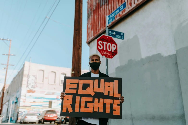 a man holding a sign that says equal rights, by Julia Pishtar, trending on pexels, black arts movement, los angeles ca, view from the streets, posters on the walls, photography of kurzgesagt