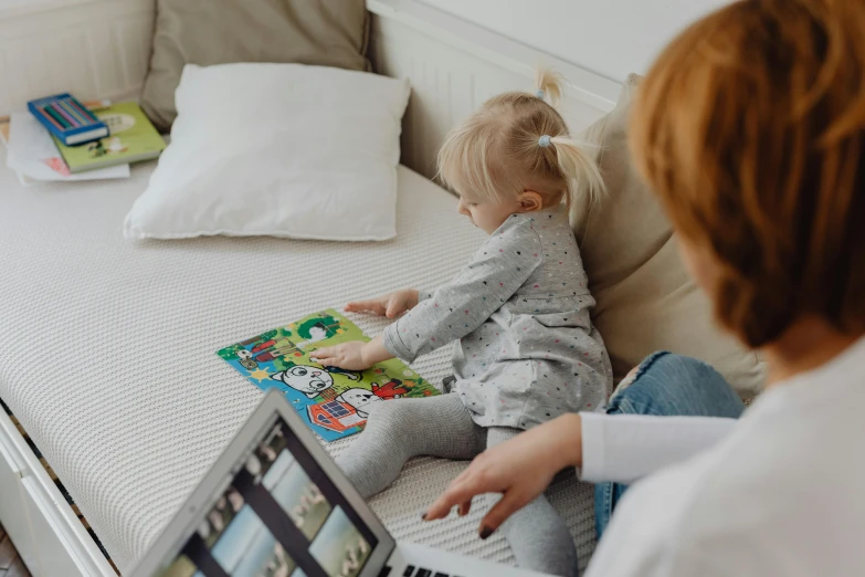 a little girl that is sitting on a bed with a laptop