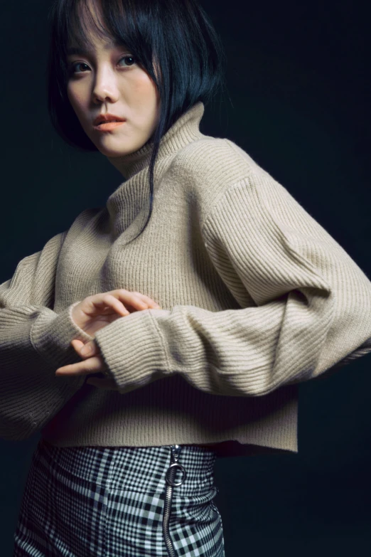 a woman standing in front of a black background, an album cover, inspired by Gao Cen, wearing casual sweater, sui ishida with black hair, at a fashion shoot, loosely cropped