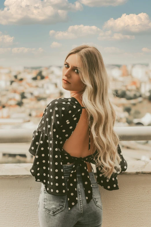 a woman standing on a balcony with her back to the camera, an album cover, trending on pexels, polkadots, long blonde hair and large eyes, wearing a cropped top, city backdrop