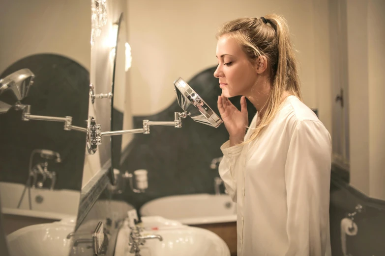 a woman brushing her teeth in front of a mirror, by Julia Pishtar, pexels, evening lighting, defined jawline, wearing a grey robe, teenage girl