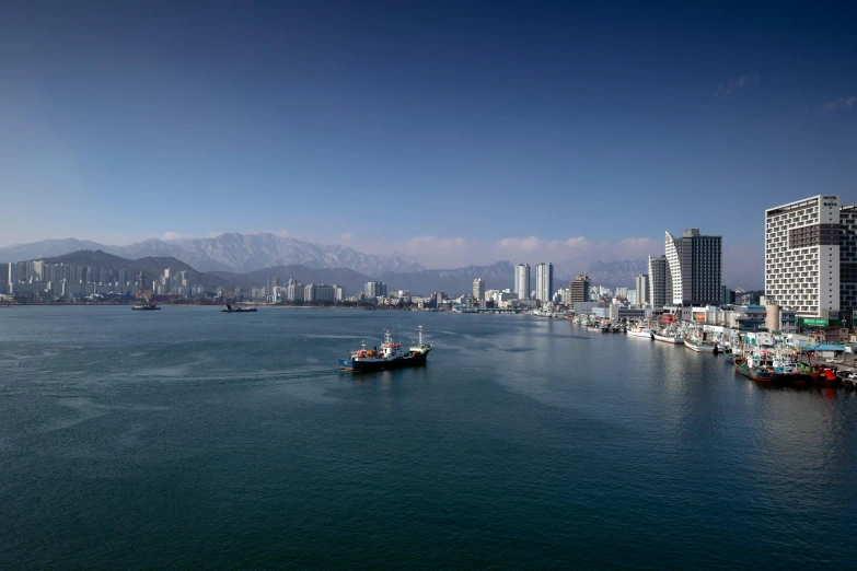 a large body of water with a boat in it, a tilt shift photo, inspired by Kōno Michisei, pexels contest winner, hurufiyya, city panorama, mountains and ocean, shipping docks, 4k photo gigapixel