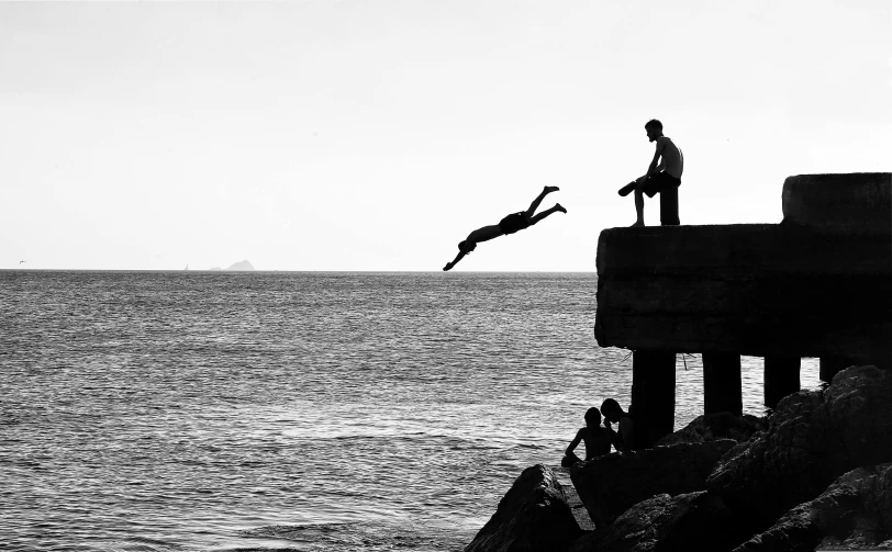 a man jumping off a pier into the ocean, a black and white photo, by Nadir Afonso, pexels, people falling off a playground, ffffound, people angling at the edge, parkour