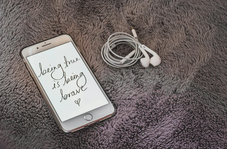 a cell phone sitting on top of a furry rug, by Robbie Trevino, trending on pexels, happening, flowing lettering, earbuds, beautiful being, saying