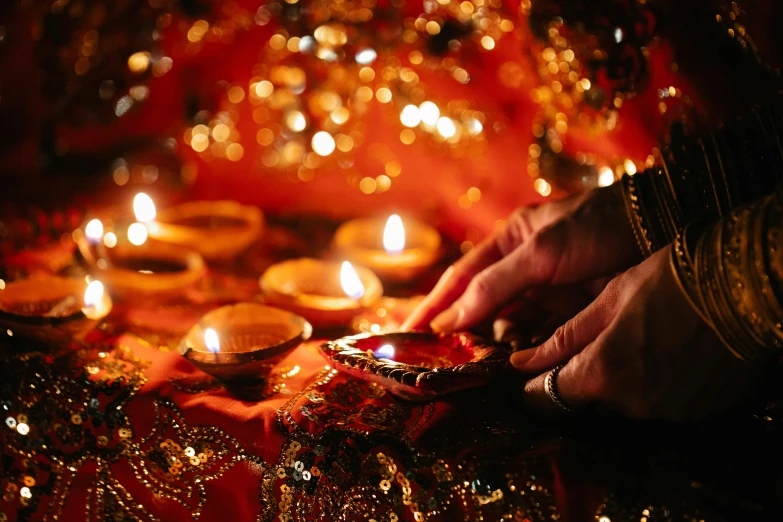 a close up of a person lighting candles, by Julia Pishtar, hindu ornaments, sequins, light red and orange mood, rectangle