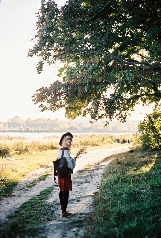 a woman walking down a dirt road next to a tree, near a lake, kodak portra film, ukrainian girl, portrait featured on unsplash