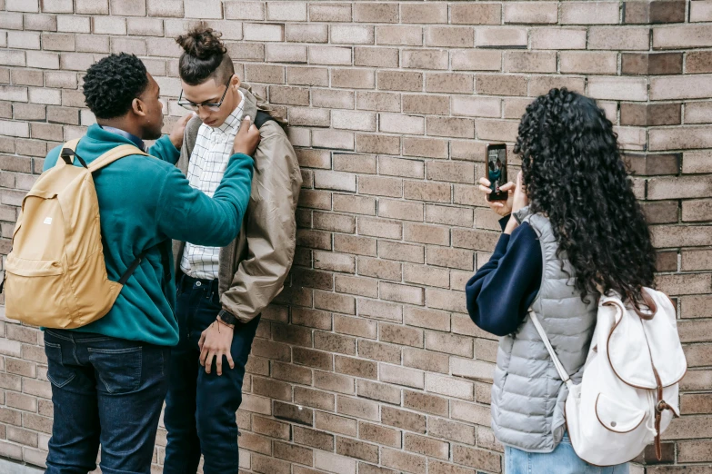 a group of people standing next to a brick wall, a photo, trending on pexels, black teenage boy, woman holding another woman, bullying, professional iphone photo