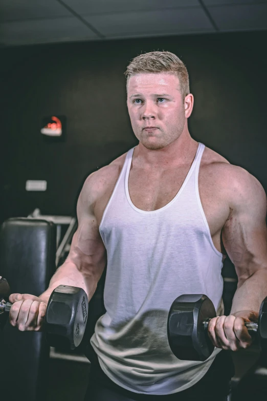 a man holding two dumbbells in a gym, an album cover, by Ryan Pancoast, reddit, intense albino, headshot profile picture, attractive beefy man, wearing a tanktop