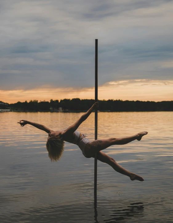 a woman hanging upside down on a pole in the water, by Grace Polit, trending on vsco, at twilight, metal bikini, near a lake