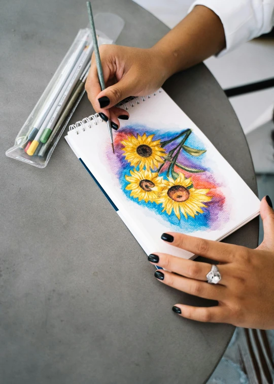 a woman is drawing sunflowers on a piece of paper, a color pencil sketch, inspired by artist, trending on pexels, intricate oil pastel glow, holding notebook, colored in, molotow premium color palette