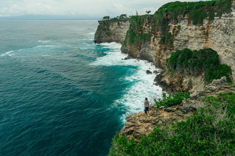 a man standing on top of a cliff next to the ocean, by Daniel Lieske, pexels contest winner, indonesia national geographic, lush surroundings, wall of water either side, hunting