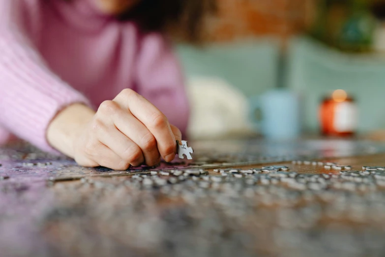 a person placing a piece of puzzle on a table, by Jessie Algie, pexels contest winner, hyperrealism, looking towards camera, on a canva, thoughtful