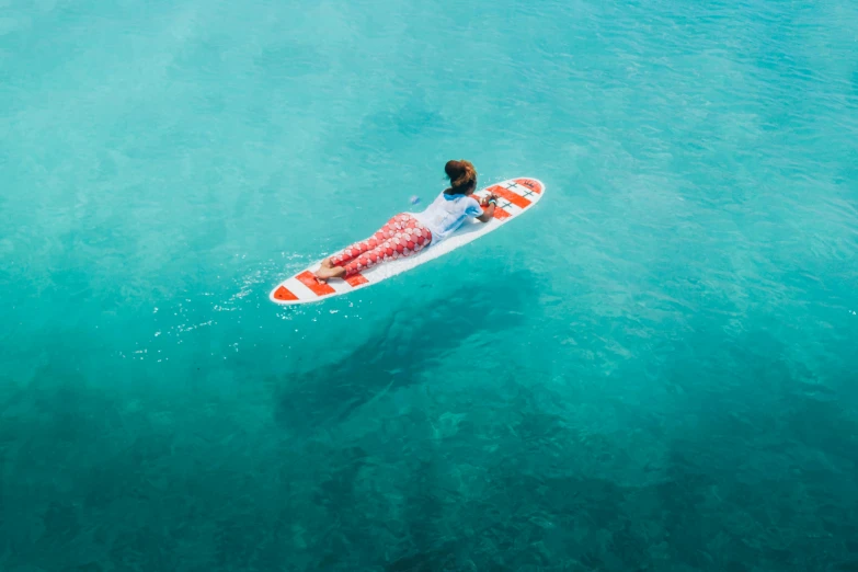 a man riding on top of a surfboard in the ocean, pexels contest winner, female floating, azure and red tones, flat lay, 5 7 9