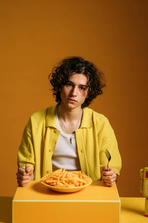 a man sitting at a table with a plate of food, an album cover, by irakli nadar, trending on pexels, wavy hair yellow theme, androgynous person, rebecca sugar, teen boy